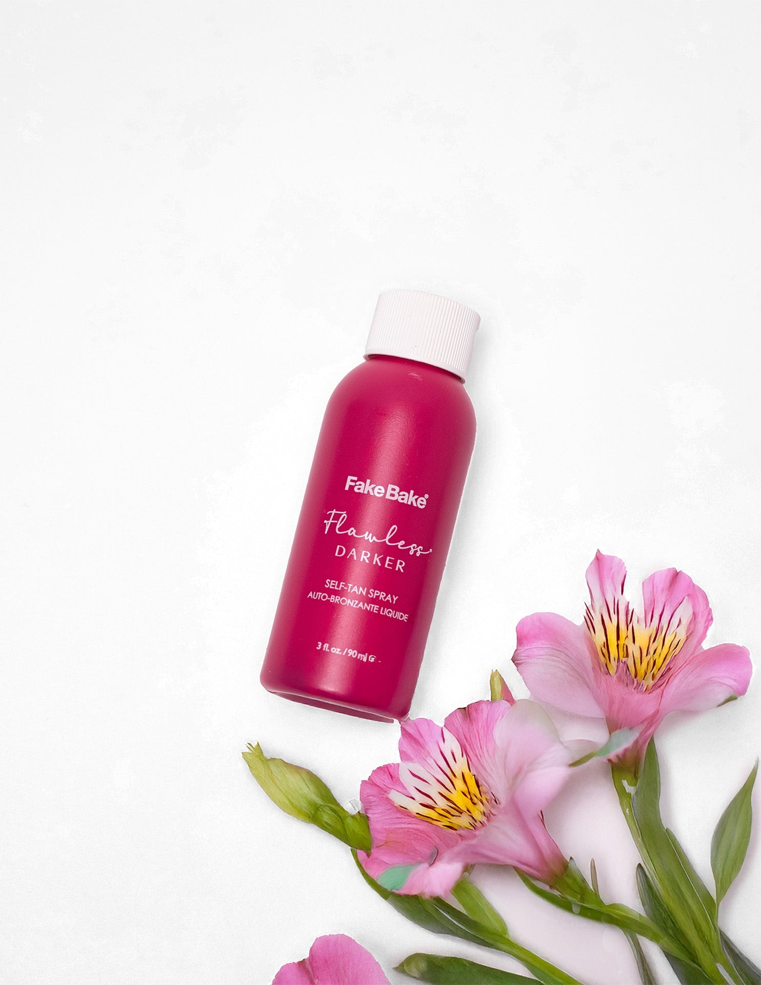 Pink mini bottle of Flawless Darker tanner with white lid. Pink flowers with green stems are nearby.