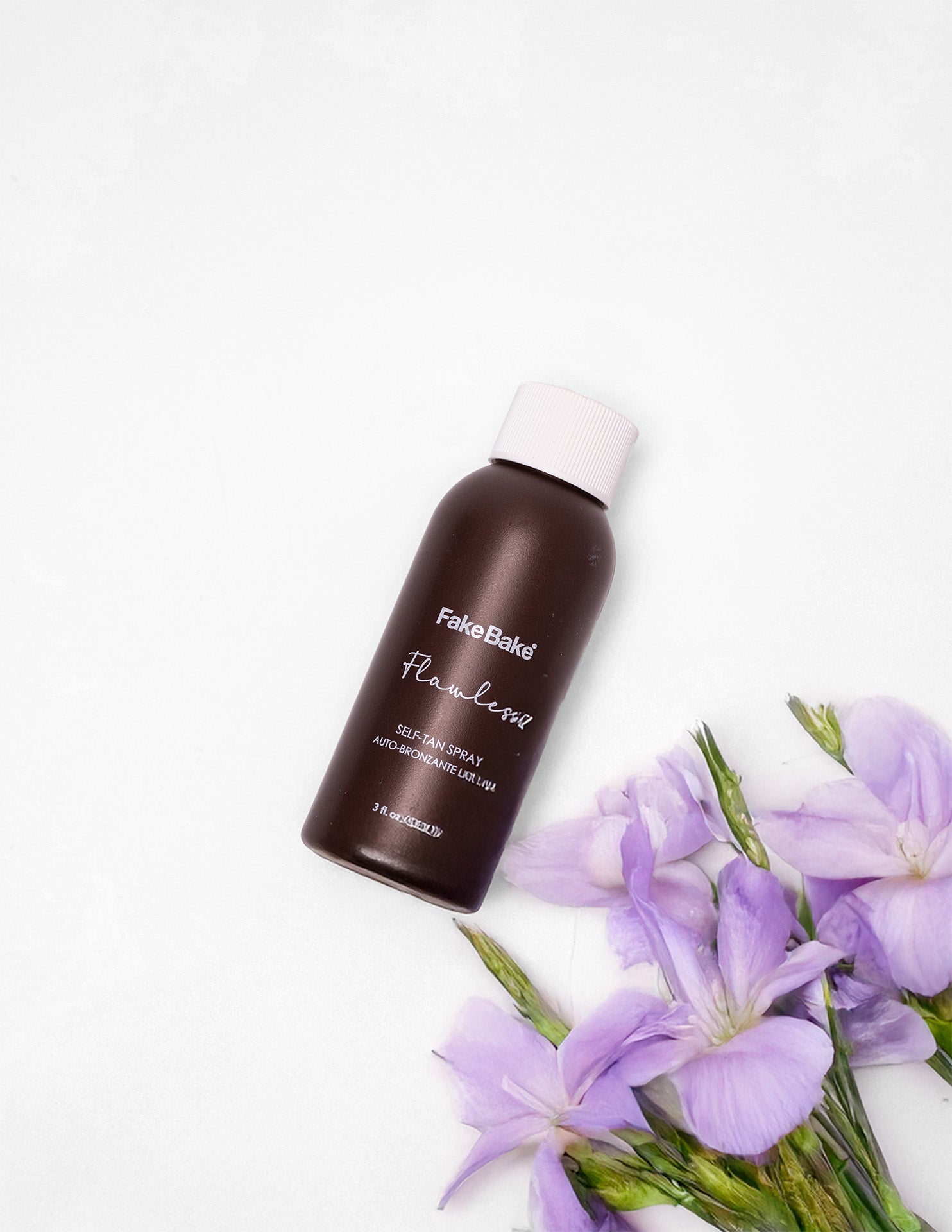 small brown bottle of Flawless tanner with white lid. Purple flowers with green stems are nearby.