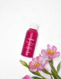 Pink mini bottle of Flawless Darker tanner with white lid.  Pink flowers with green stems are nearby.